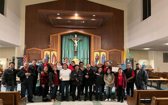 Group of people posing in front of a church altar with a large cross and green curtains