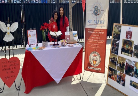 Two people behind a red-and-white table display at a St. Mary booth with banners and brochures