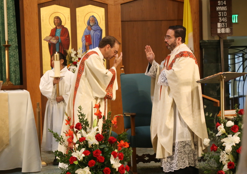 Priest blessing a man during a church ceremony, with floral decorations and altar backdrop