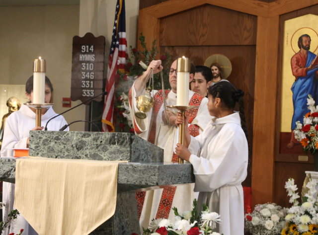 Catholic altar with clergy in white robes, candles, flowers, and religious icons during a church service