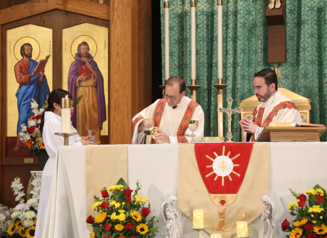 Three clergy at an altar during a church service, with candles, flowers, and religious icons.