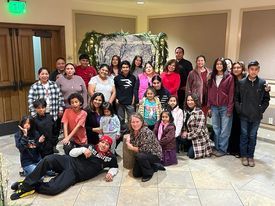 Group of people posing indoors in front of a decorated archway, several seated in front and others standing behind.