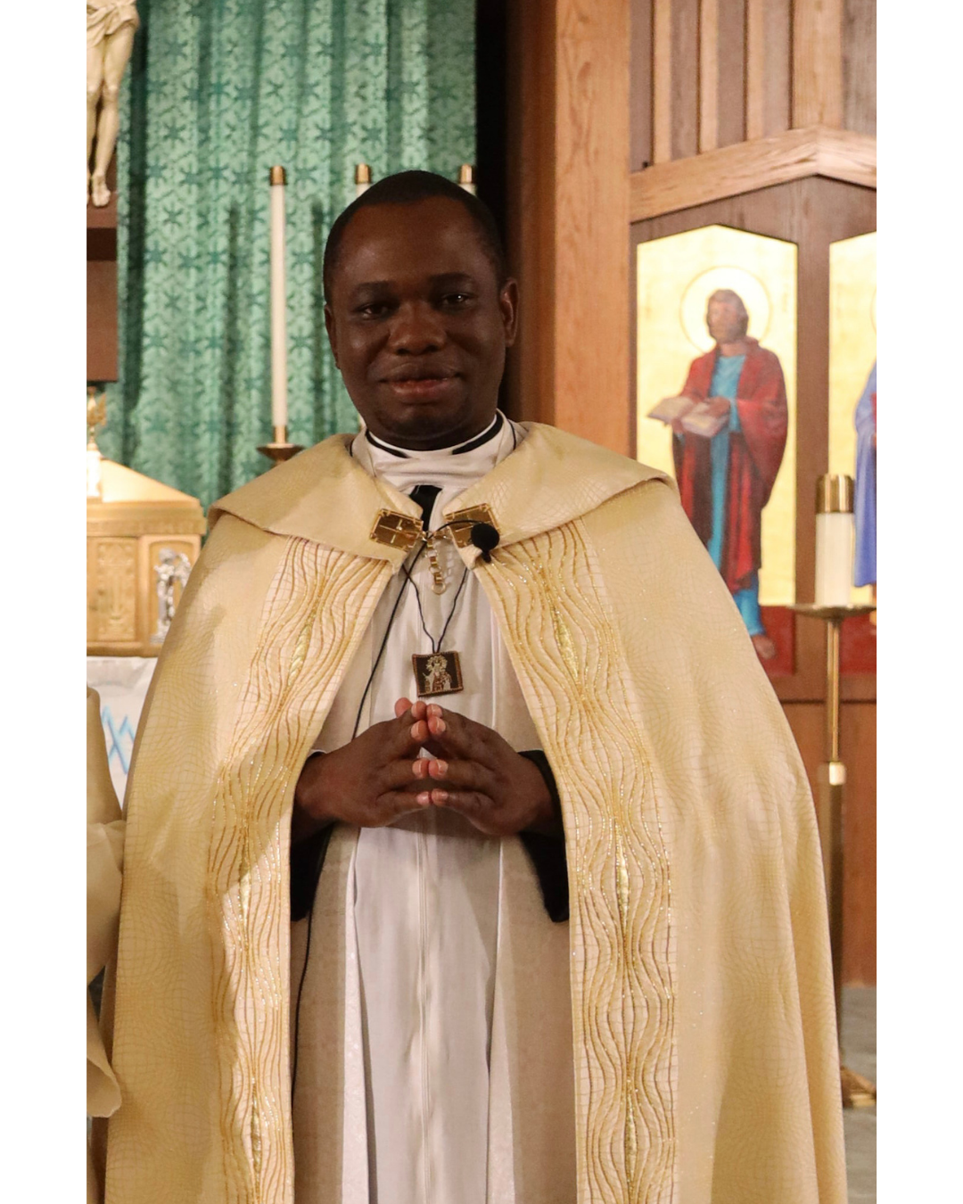 Man in white clergy vestments, posing in front of the St. Mary church altar. 