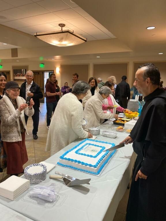 People gathered around a table with blue-and-white cakes at an indoor celebration