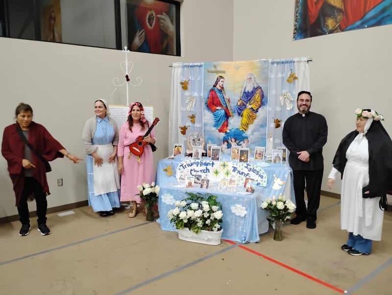 People posing beside a decorated display with colorful artwork, flowers, and a table in a hall