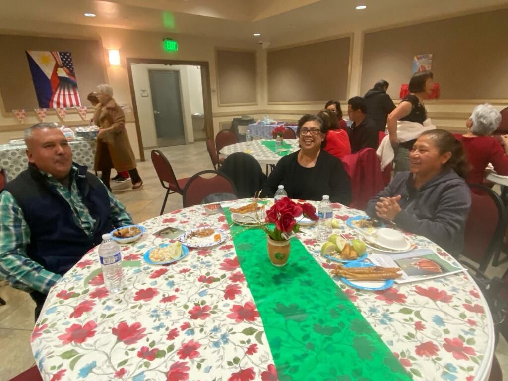 People seated at a decorated banquet table in a community hall, smiling and chatting.