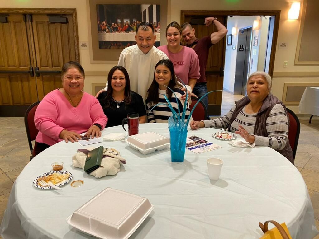 Group of six smiling people gathered around a table with snacks and a blue centerpiece in a kitchen.
