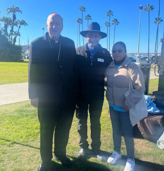 Three people standing on a sunny lawn near palm trees, posing for a photo