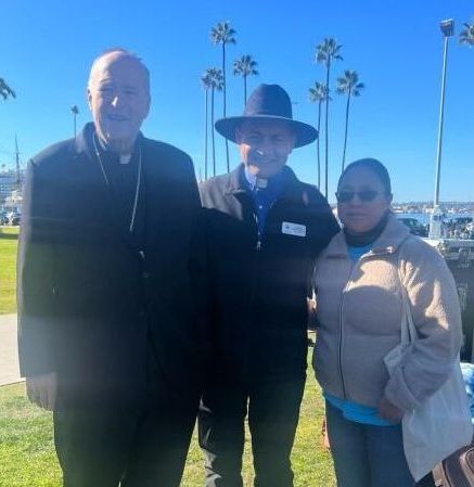 Three people standing together outdoors by a marina on a sunny day.