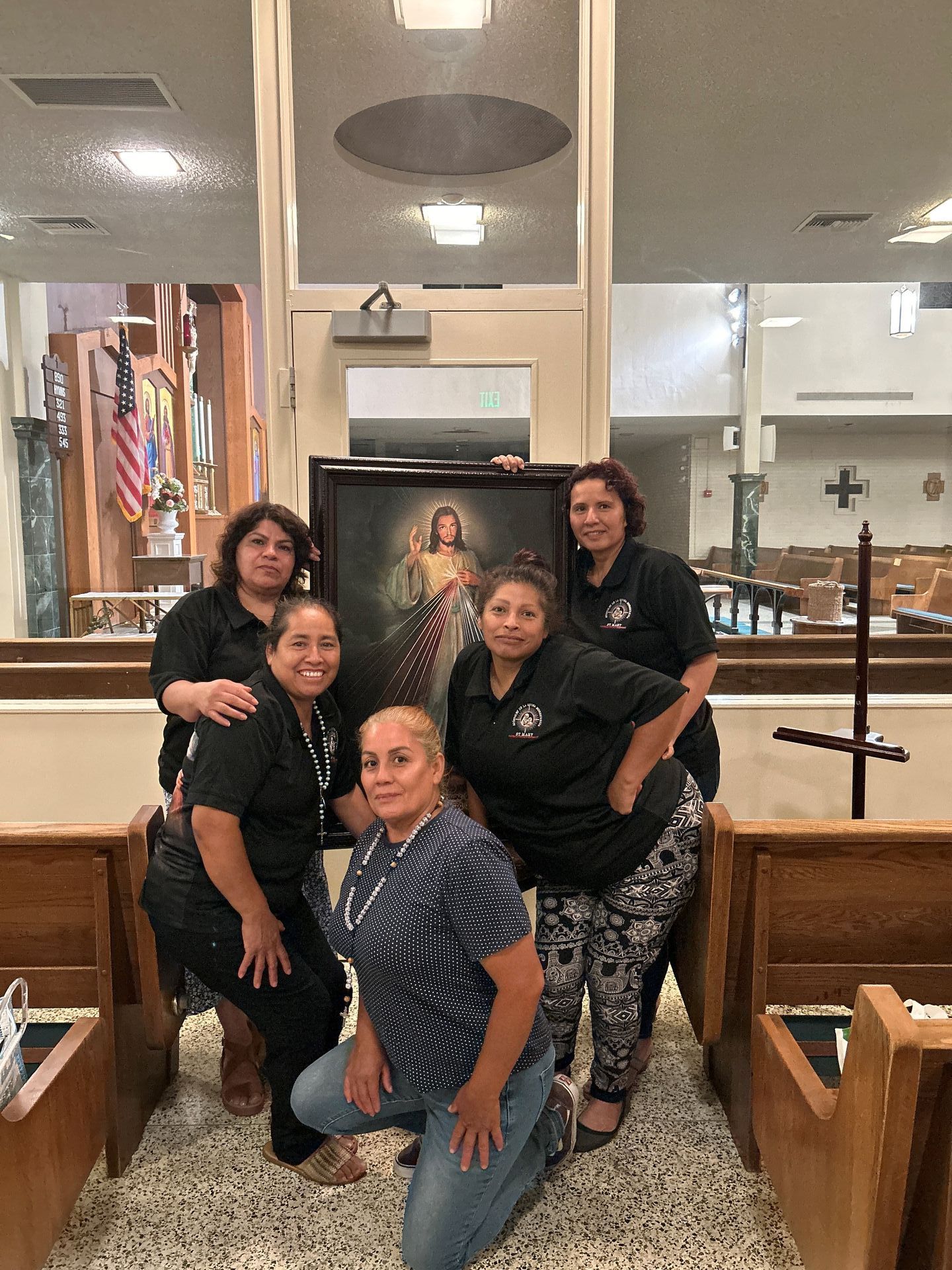 Five people pose inside a church in front of a framed portrait and wooden pews.