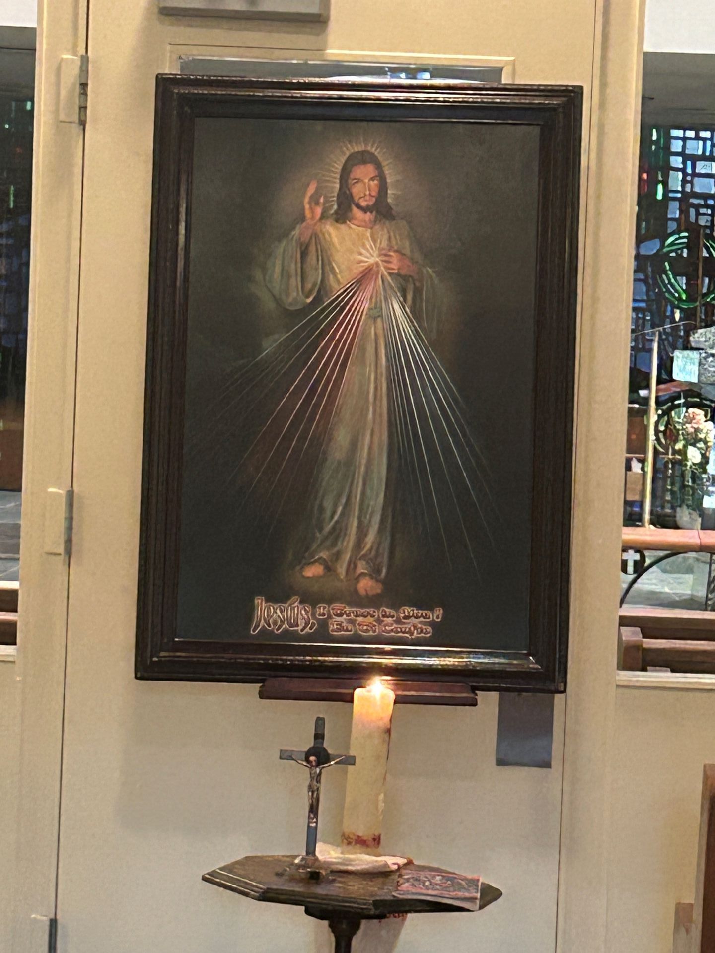 Religious painting of Jesus with rays, framed on a wall above a lit candle and small altar table
