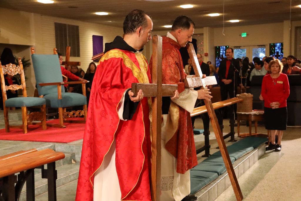 Two clergy in red robes stand at a church altar, one holding a long staff.