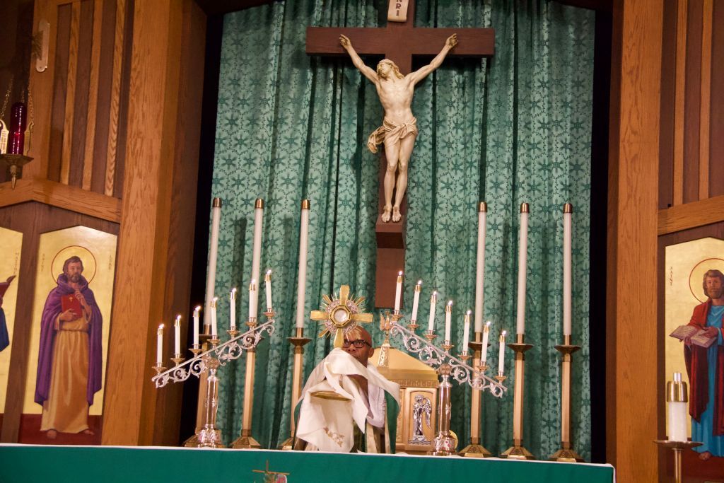 Catholic altar with crucifix, green curtains, candles, and a priest in vestments during Mass