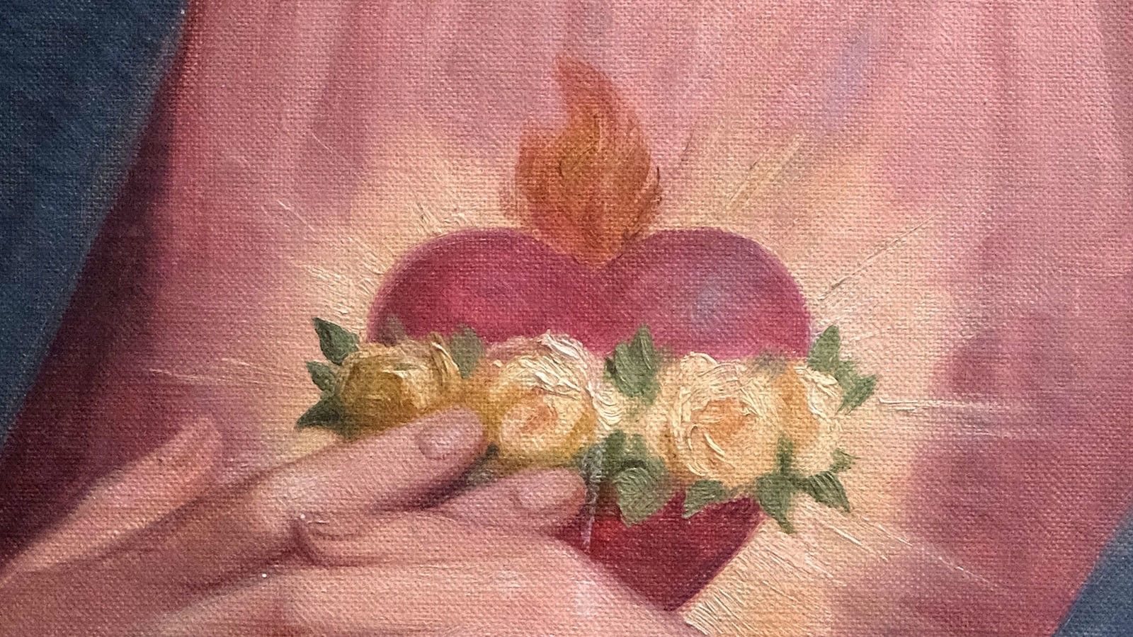 Hands holding a small heart-shaped floral arrangement with pink and yellow flowers on a pink background