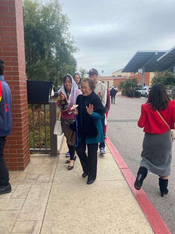 People walking outdoors on a school campus near a brick building and solar panels.