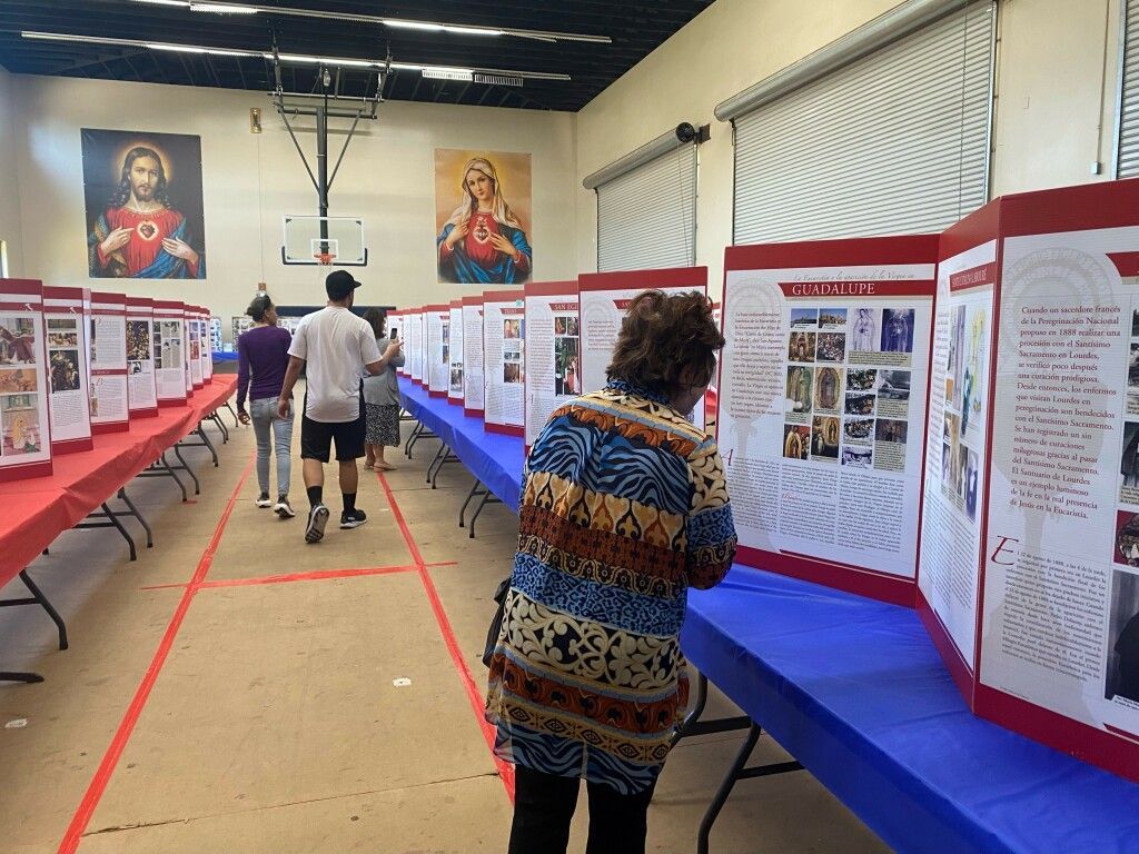 Exhibit hall with poster boards on blue tables and visitors walking down a central aisle