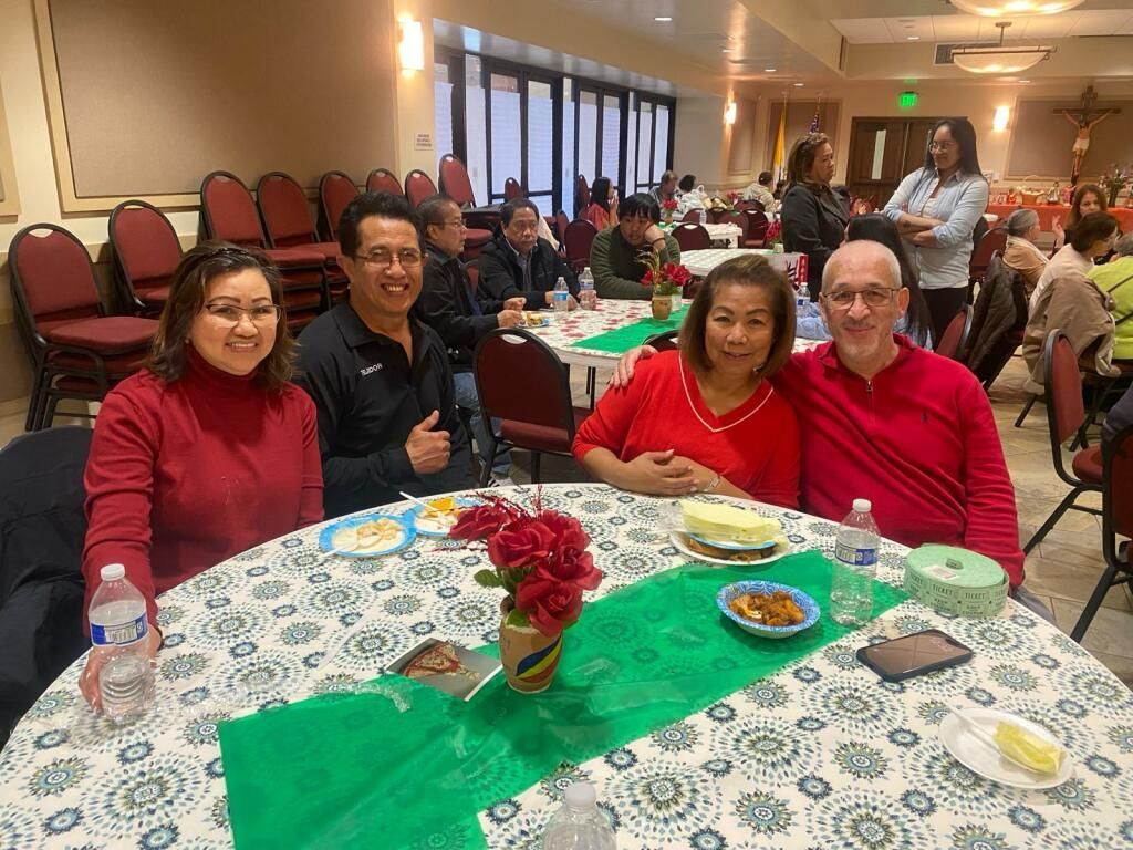 Four people seated at a banquet table in a decorated dining hall, smiling at the camera