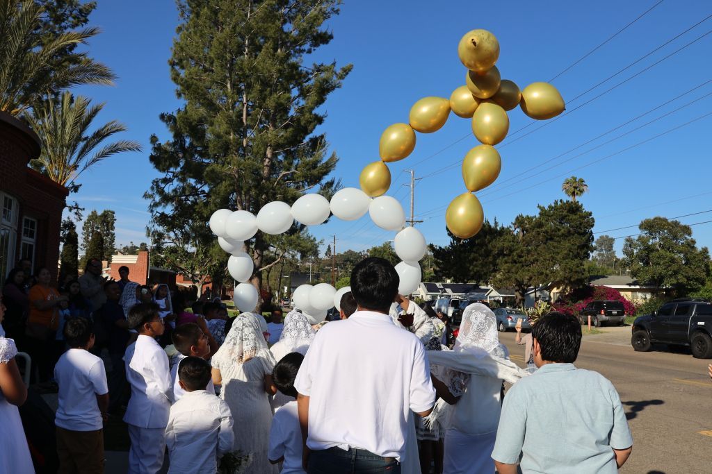 People in white shirts gather around a balloon sculpture of a person in a sunny outdoor area