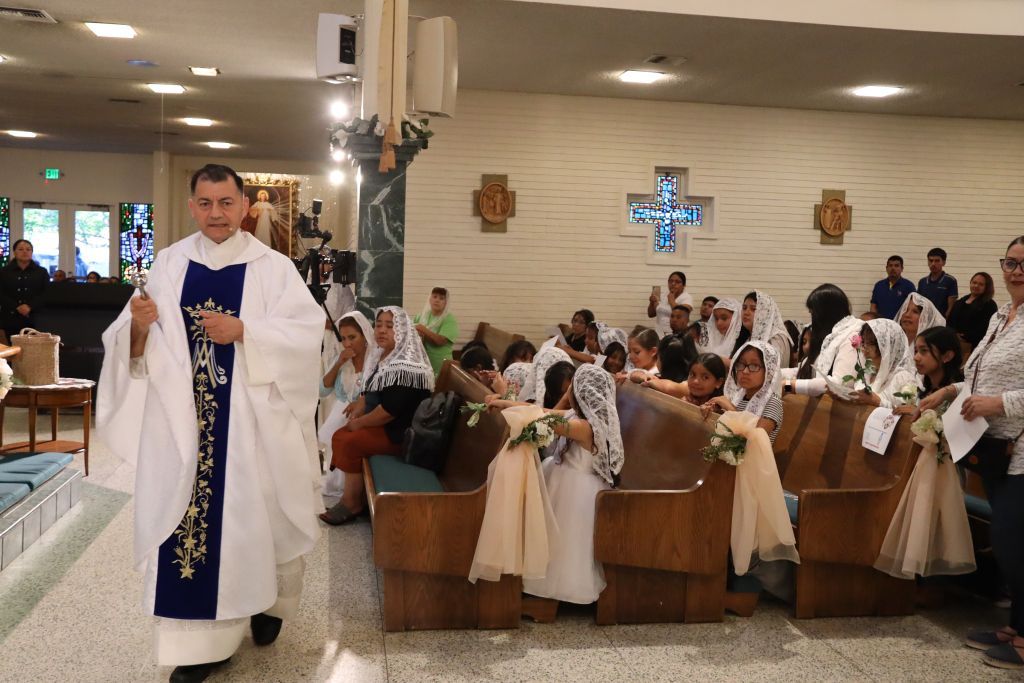 Priest in white vestments blessing congregants kneeling in a church service