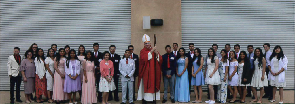Group of people posing outdoors against a metal wall, centered around one person in a red robe.