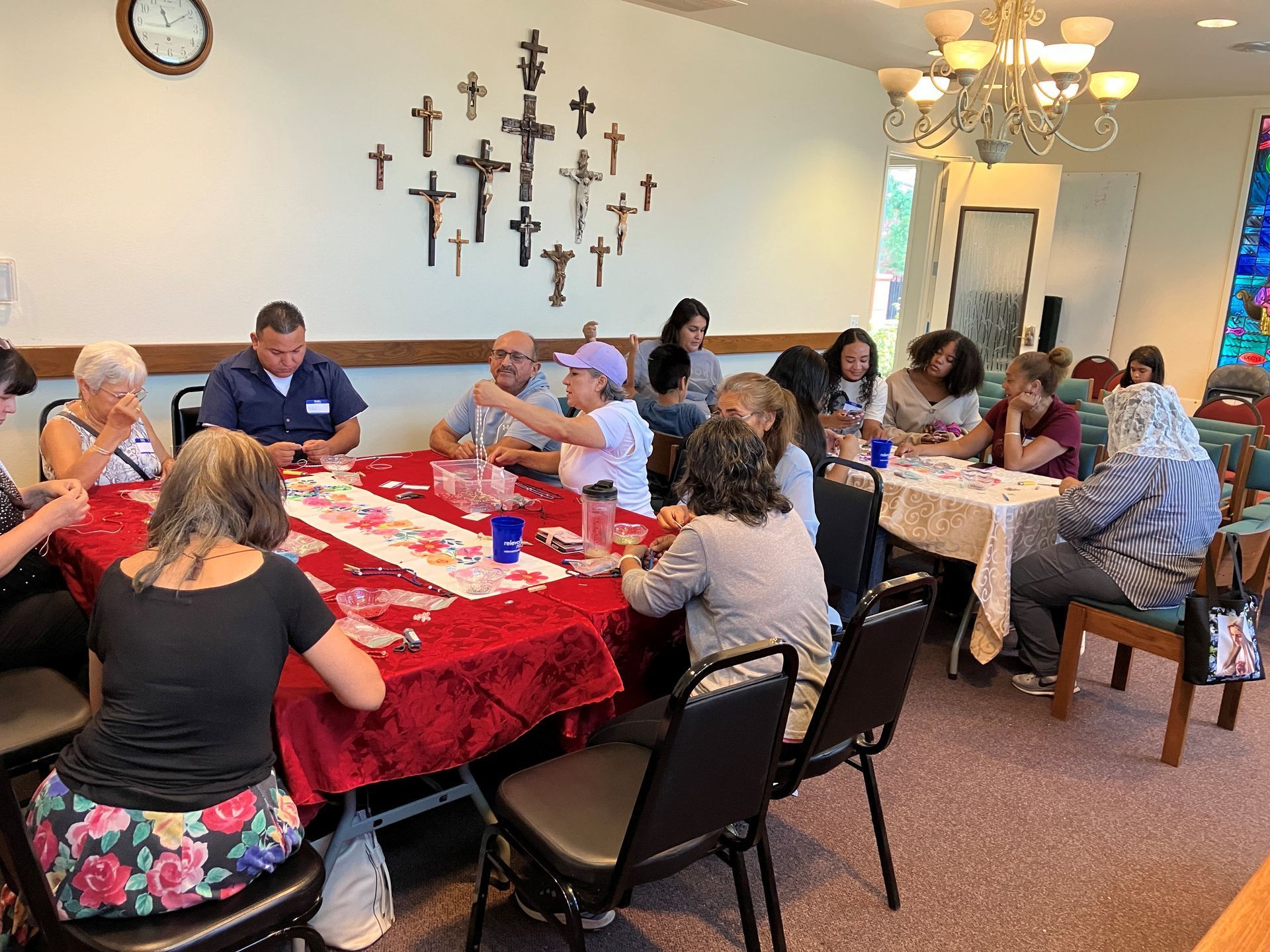 People seated around a banquet table in a church hall, talking and eating under wall crosses.