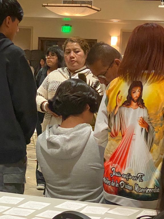 People standing and talking in a hotel hallway, with one person in a white hoodie facing away.
