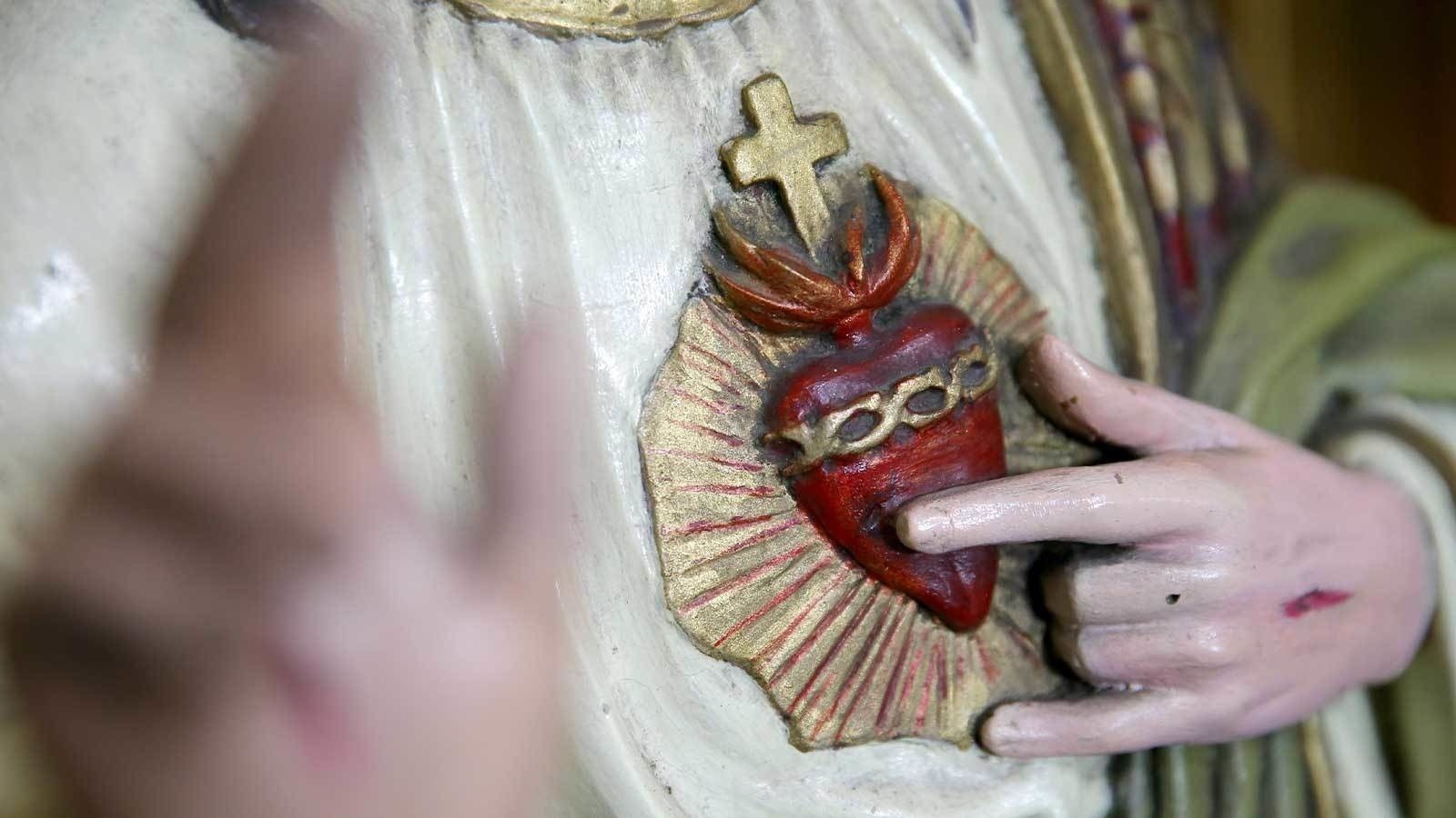 Hand touching a red heart-shaped religious pendant with a cross on white fabric