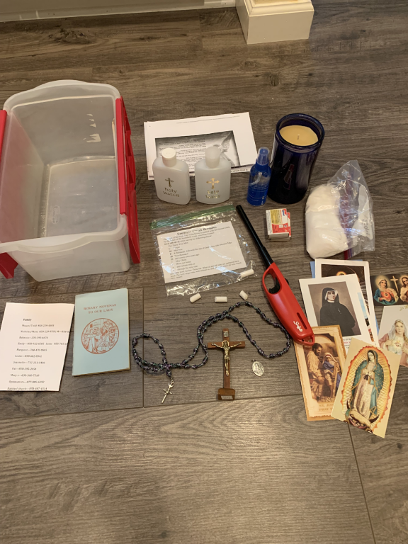 Assorted items on a floor, including a plastic bin, candles, jewelry, prayer cards, and small trinkets
