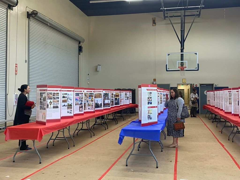 Poster displays in a gymnasium with tables and a basketball hoop, people viewing exhibits.