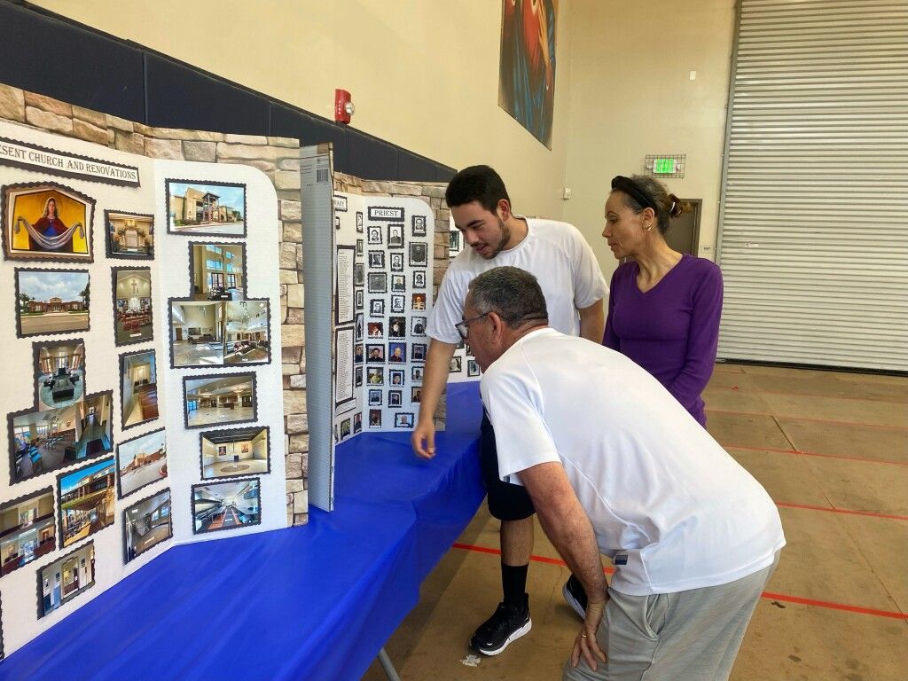 Three people viewing photo displays at an indoor exhibit with blue table coverings