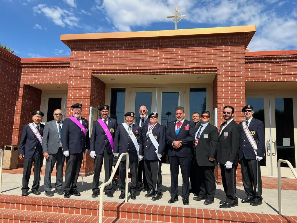 Group of officials in suits posing outside a brick building under a blue sky.
