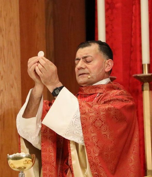Priest in red vestments raises a communion wafer during a church service