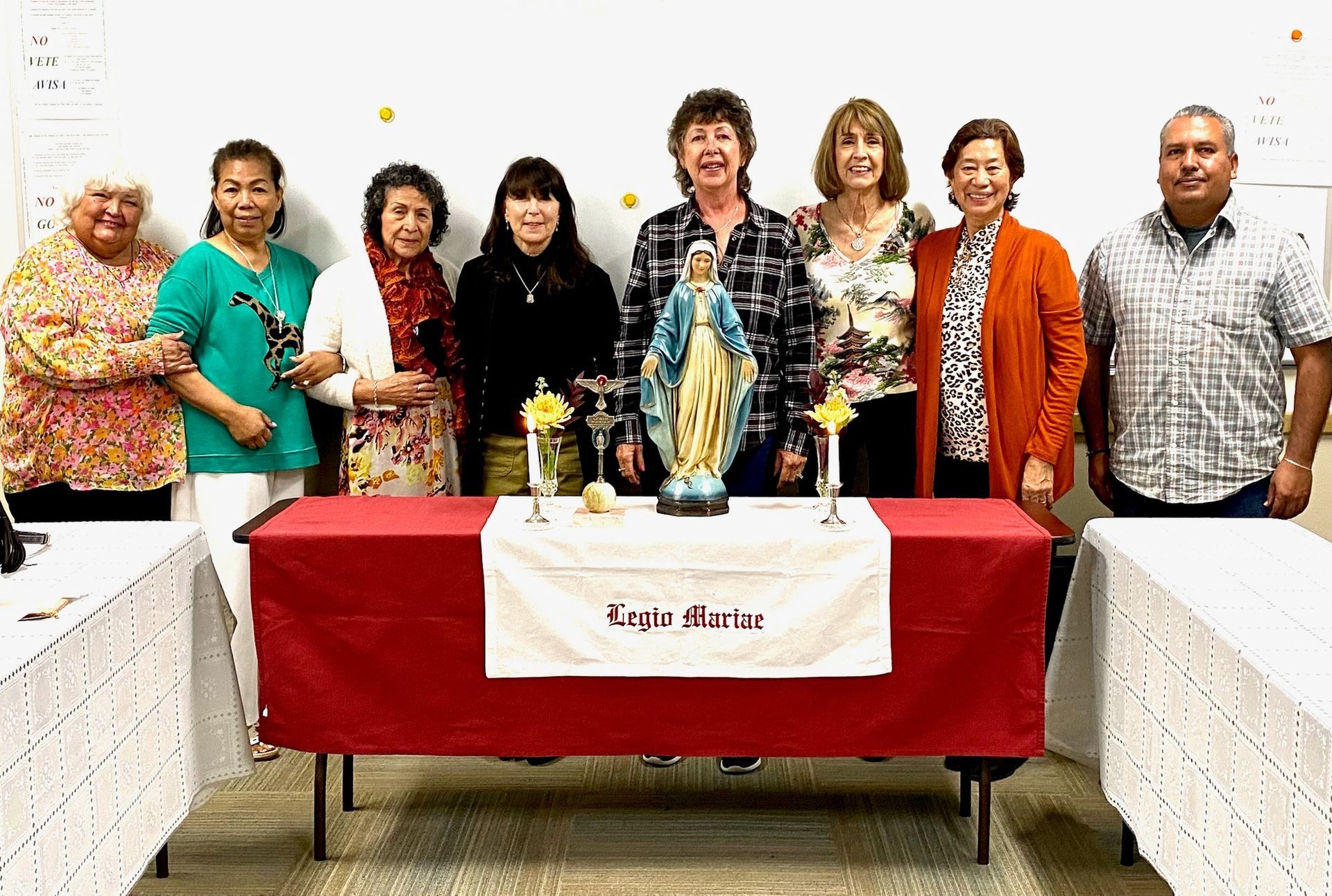 Group posing behind a red-covered table with decorated items at a community event