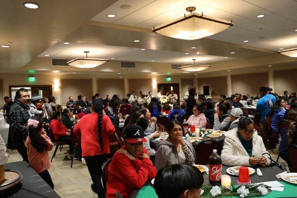 Crowded banquet hall with people seated at tables and mingling under ceiling lights