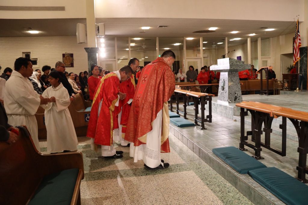 Clergy in red robes process inside a church toward the altar during a service
