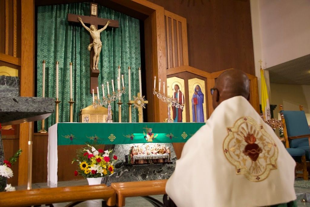 Catholic altar with crucifix, green cloth, flowers, and a white robe in the foreground