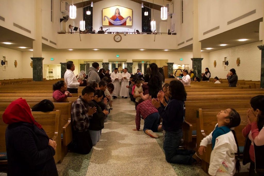 People seated in church pews during a service, facing the altar and choir loft.