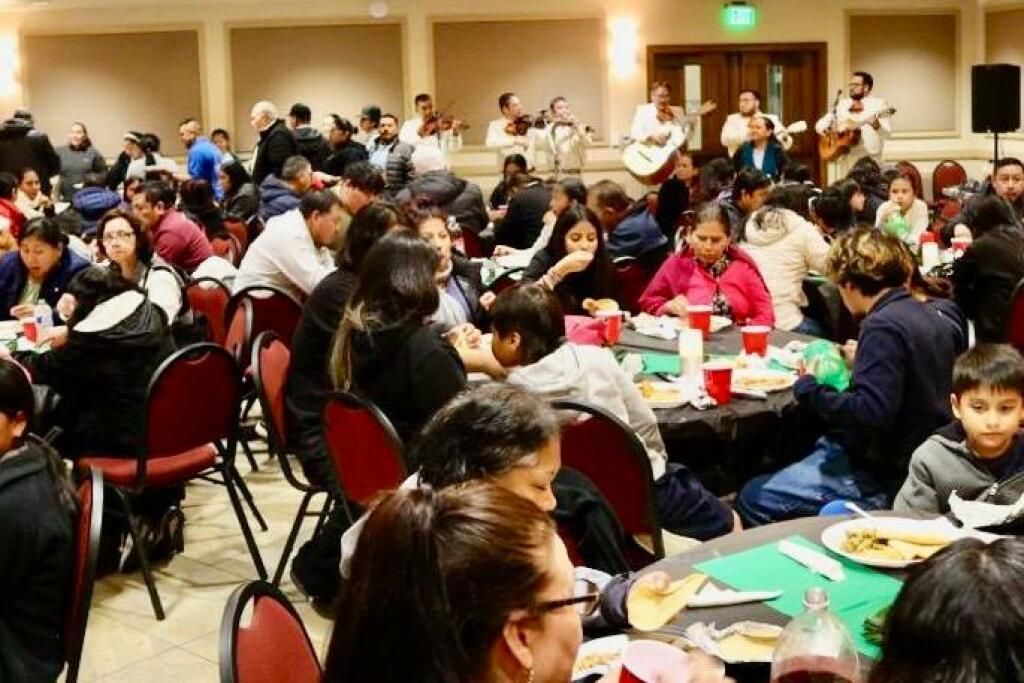 Crowded banquet hall with people seated at round tables, eating and socializing during an event
