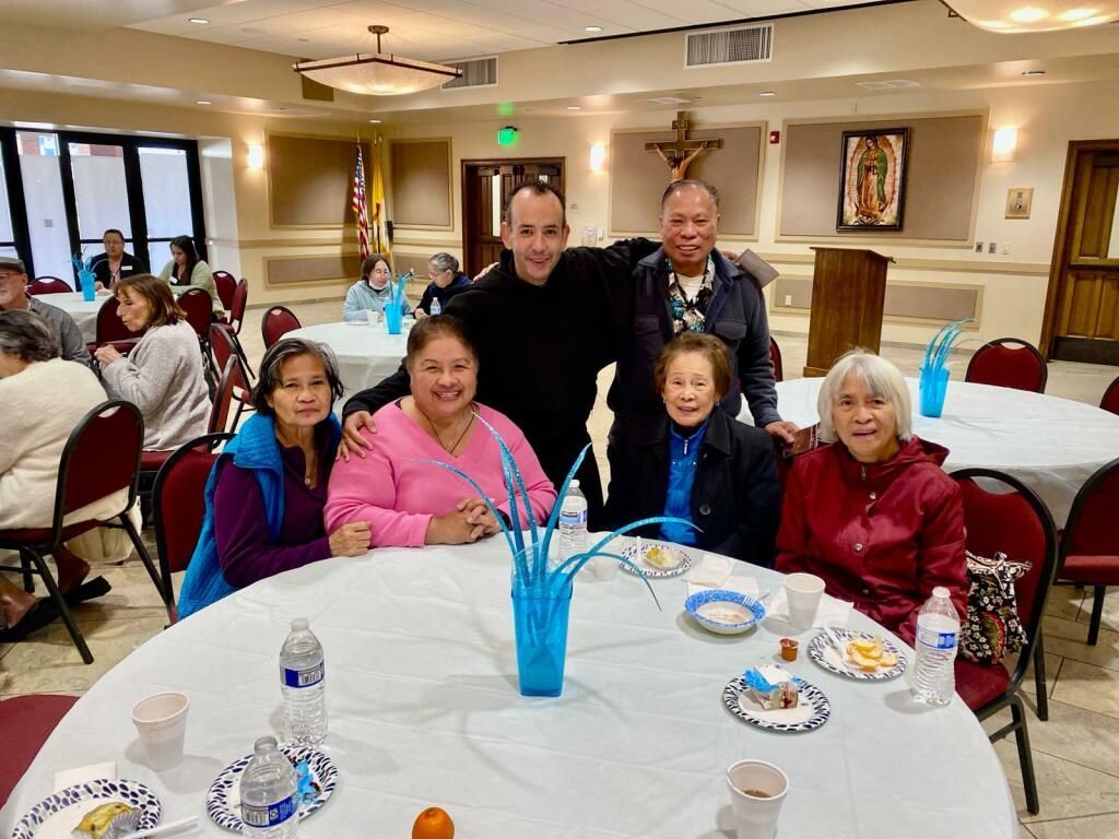 Five people seated at a round table in a banquet hall, smiling during a social gathering.