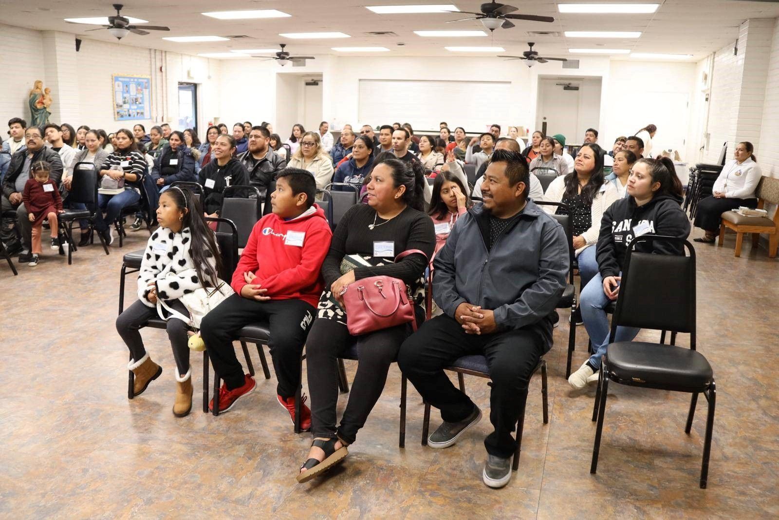 Audience seated in a community hall, listening to an event or presentation