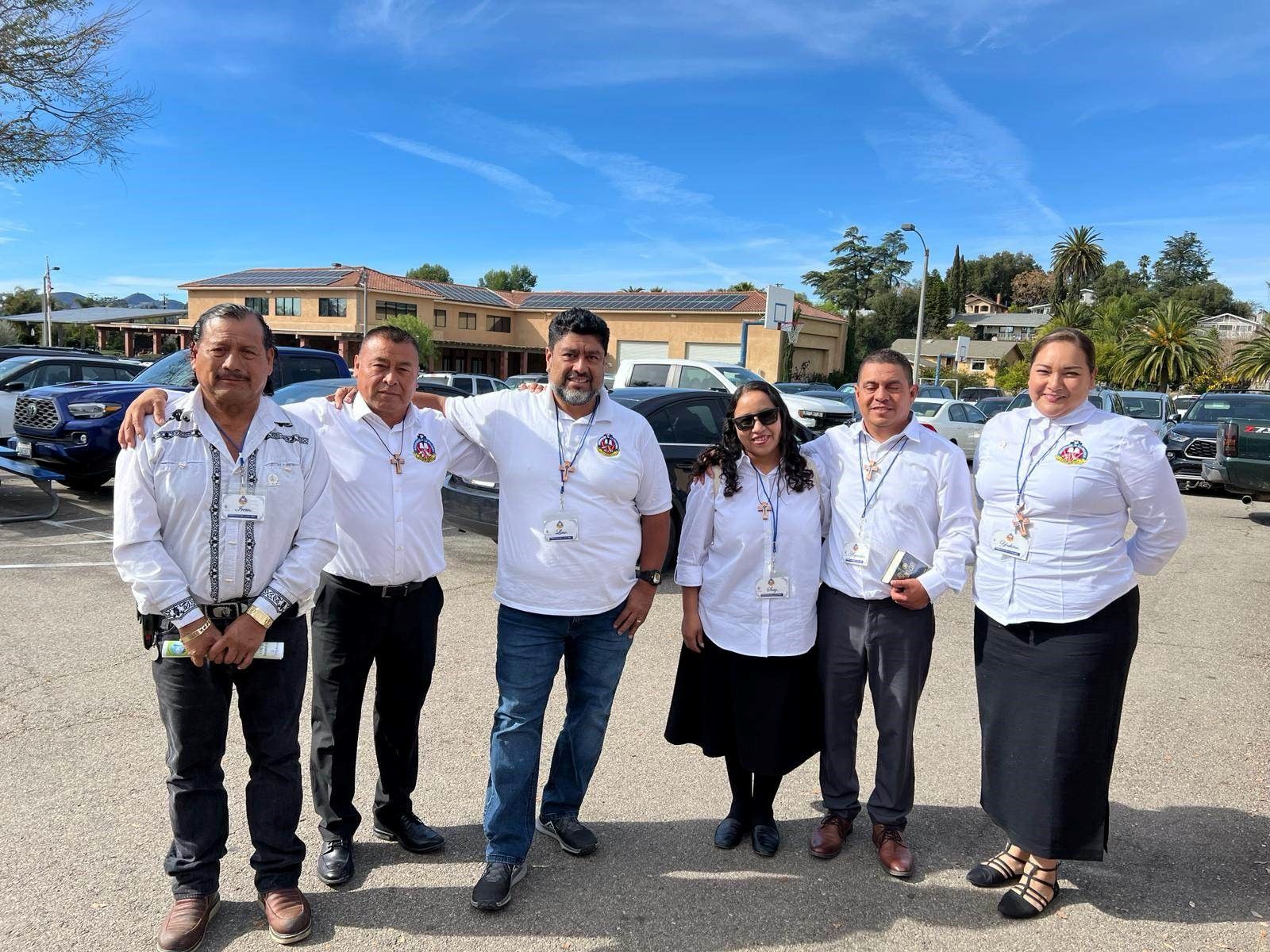 Six people in white shirts standing together in a parking lot on a sunny day.