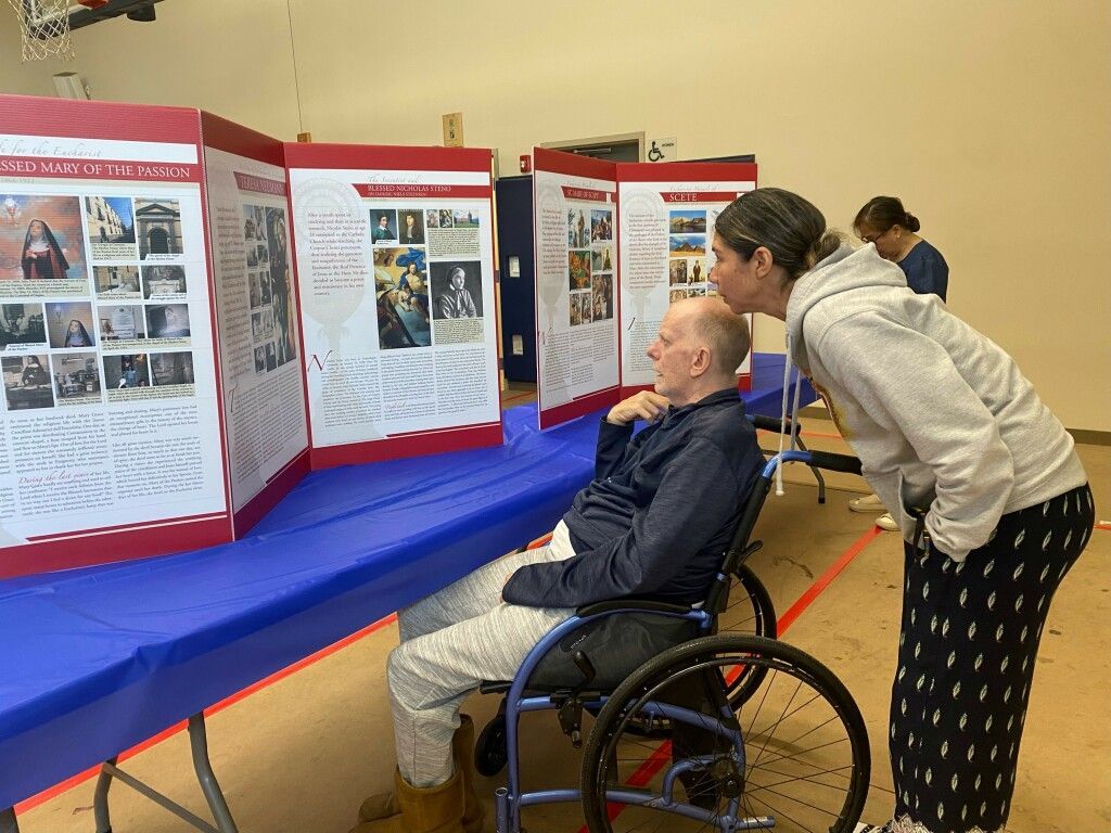 Two people viewing poster displays at a community exhibit, one in a wheelchair.
