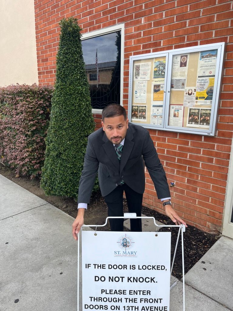Man in a dark suit holding a sign outside a brick building entrance.