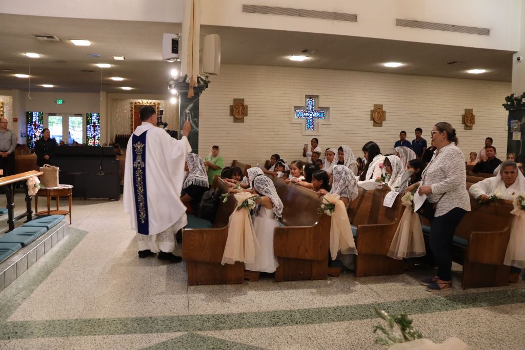 Priest in white robe speaking to seated congregation inside a church decorated for a ceremony