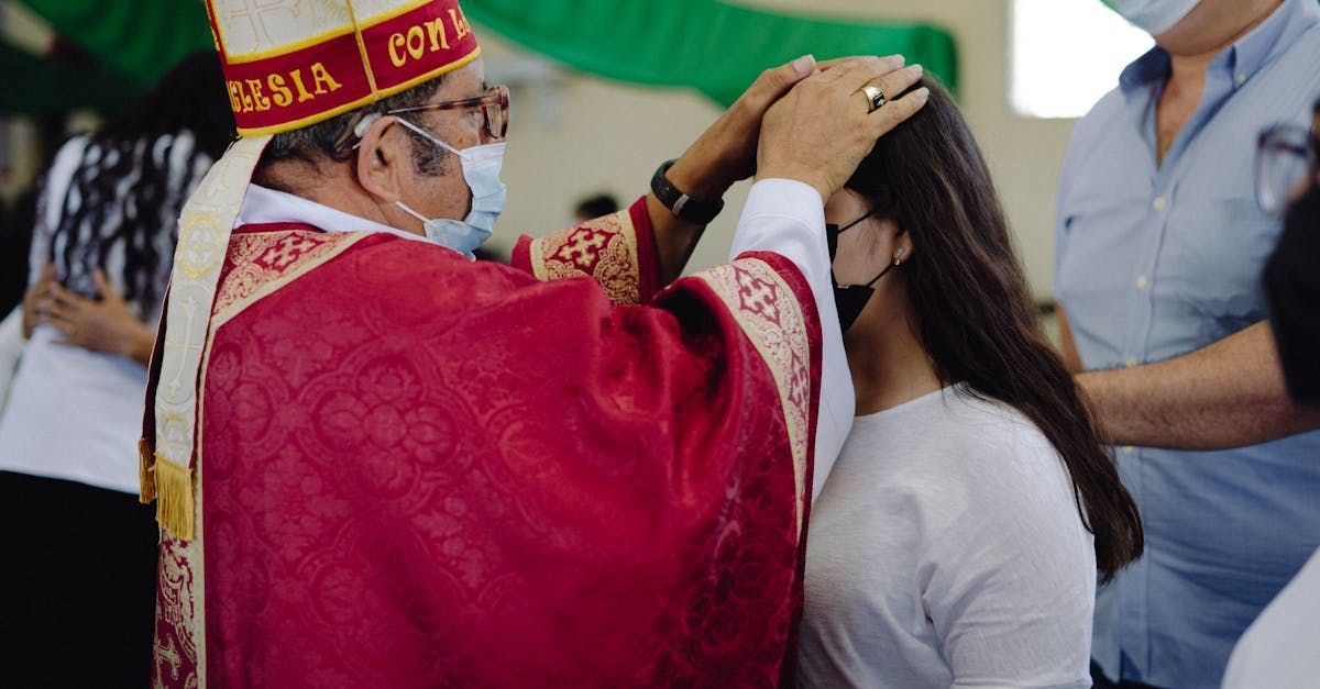 A bishop in a red robe places a ceremonial mark on a woman’s forehead during a blessing