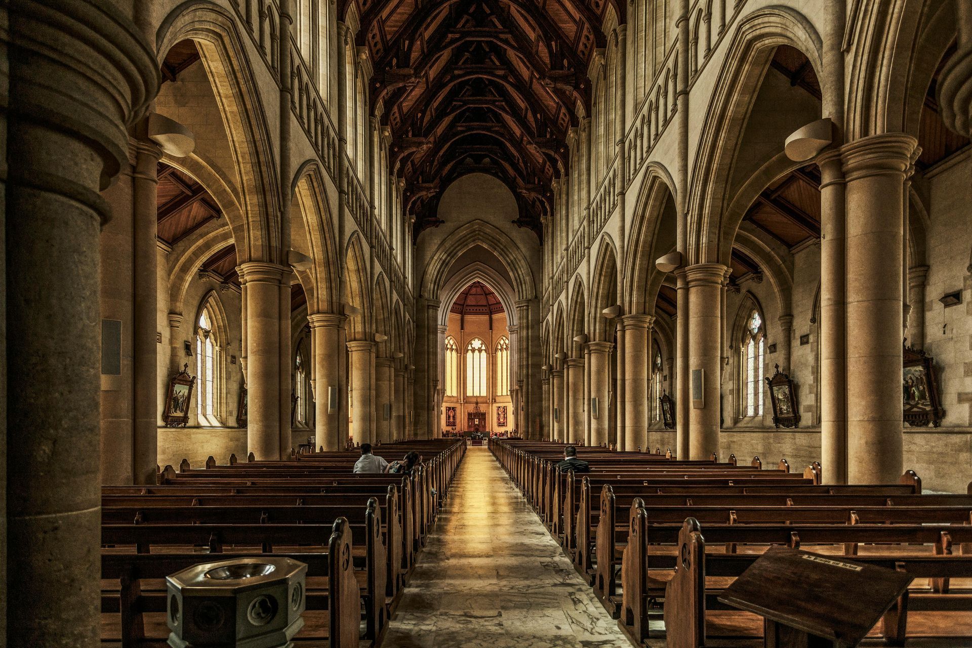 Empty cathedral nave with rows of wooden pews and a glowing altar at the far end