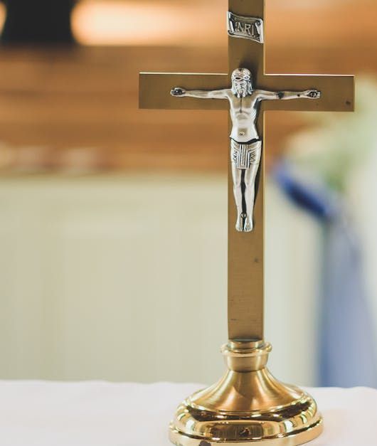 Small silver crucifix on a brass stand, centered against a softly blurred background.