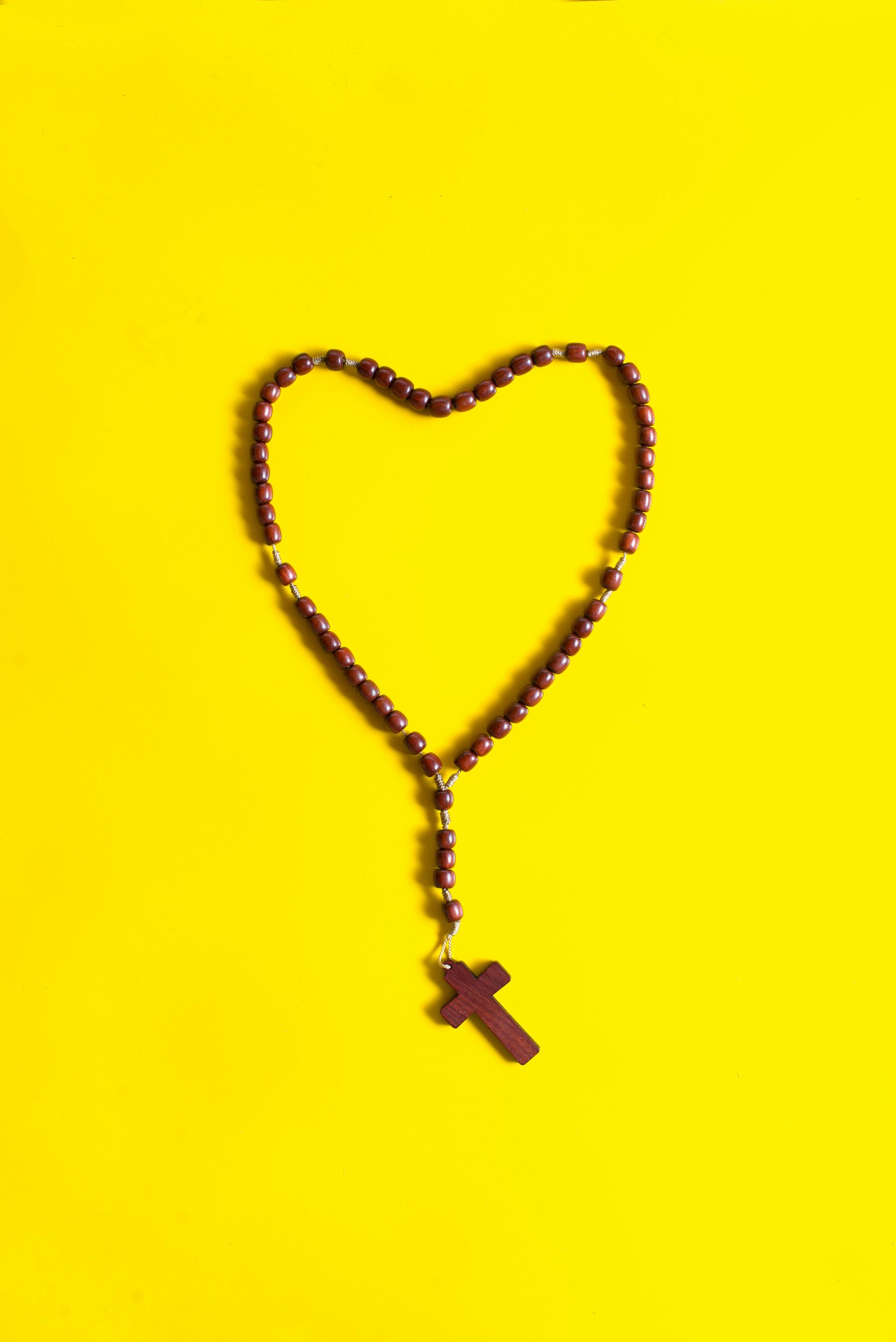 Rosary arranged in a heart shape on a bright yellow background
