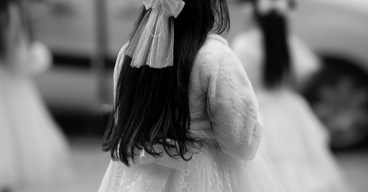 Black-and-white scene of a child in a white dress with a bow, seen from behind among other dancers