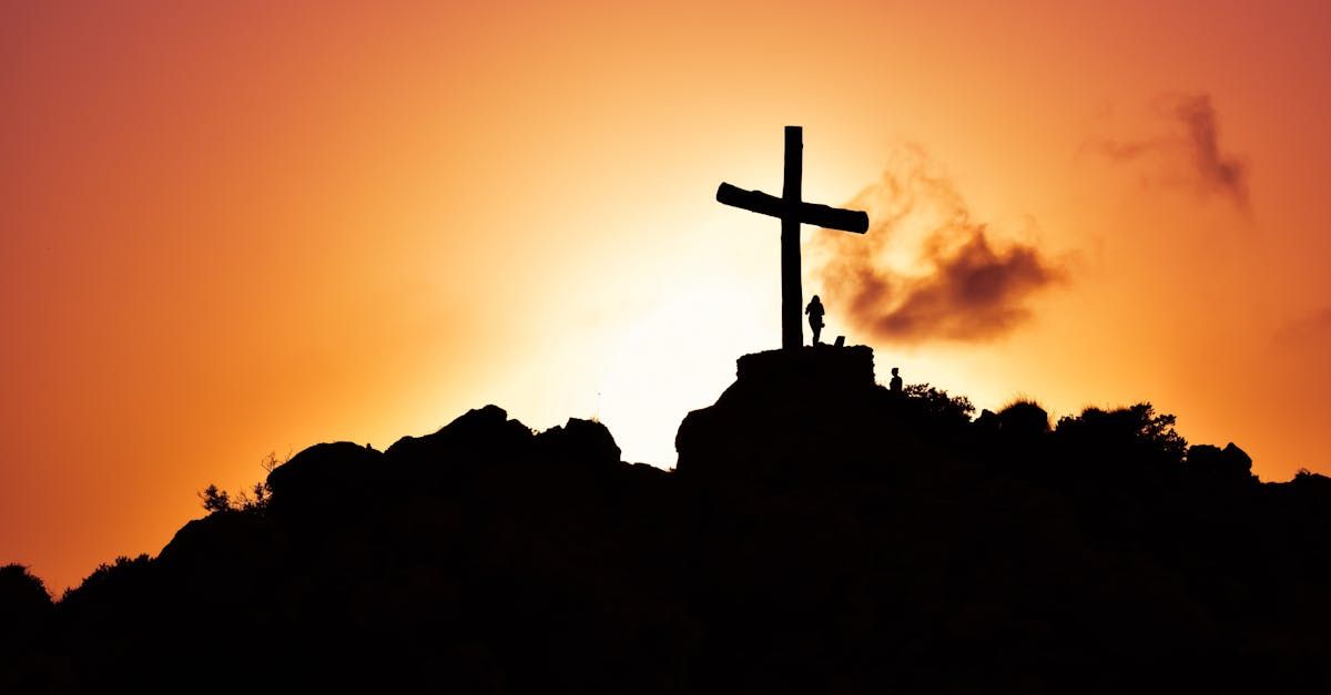 Silhouette of a cross on a hill against an orange sunset sky